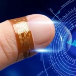 Immagine fotorealistica di un nanogeneratore ibrido flessibile BPP-HNG, sottile e trasparente, applicato su un dito umano. In primo piano, il dispositivo che si piega con il movimento del dito, con un accenno di circuiti sottili. Sullo sfondo, un'interfaccia digitale futuristica che mostra segnali energetici. Obiettivo macro 85mm, illuminazione da studio che enfatizza la flessibilità e la tecnologia integrata, profondità di campo.
