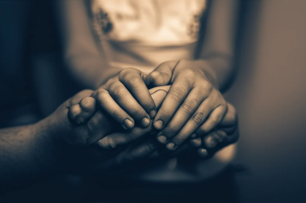 Immagine concettuale che rappresenta la vulnerabilità dei bambini e degli adolescenti messicani di fronte alla violenza interpersonale. Potrebbe essere un primo piano di mani di un adulto che proteggono delicatamente una figura stilizzata di bambino, con uno sfondo leggermente sfocato che suggerisce un ambiente domestico o comunitario messicano. Luci soffuse, colori caldi ma con un accenno di ombra per simboleggiare il pericolo. Obiettivo prime, 35mm, profondità di campo, duotone seppia e blu scuro.