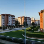 Immagine fotorealistica che mostra un contrasto tra un quartiere residenziale benestante e uno di edilizia popolare, simboleggiando le diverse percezioni pubbliche. Obiettivo 24mm, profondità di campo, luce drammatica al tramonto per enfatizzare le differenze socio-economiche.
