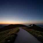 Paesaggio grandangolare, obiettivo 15mm, lunga esposizione, un sentiero tortuoso che conduce verso un orizzonte più luminoso sotto un cielo che si schiarisce, simboleggiando il percorso di recupero e sviluppo professionale dopo un trauma, tema centrale dell'articolo.