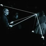 Immagine concettuale high-tech che illustra il processo di re-identificazione di persone tramite intelligenza artificiale, combinando dati da telecamere visibili e infrarossi. Figure umane stilizzate sono evidenziate attraverso diverse condizioni di luce, con linee di connessione che indicano il matching. Obiettivo prime 35mm, atmosfera film noir con contrasti accentuati, profondità di campo.