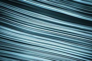 Primo piano estremamente dettagliato di una singola fibra muscolare di ratto osservata al microscopio, con le caratteristiche striature ben visibili. La fibra è illuminata in modo sottile per accentuarne la texture tridimensionale. Lente macro, focale 90mm, messa a fuoco precisa, illuminazione da laboratorio controllata, con un leggero duotone ciano e grigio per sottolineare il contesto scientifico e la profondità di campo.