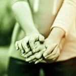 Immagine concettuale che rappresenta la complessità dell'alfa-mannosidosi e la speranza data dalla ricerca; un primo piano di mani che si sostengono, con un effetto di luce soffusa e un obiettivo da 50mm per un bokeh delicato, simboleggiando supporto e cura, con colori duotone verde e ambra.