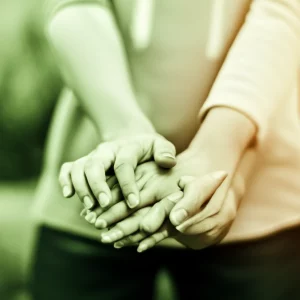 Immagine concettuale che rappresenta la complessità dell'alfa-mannosidosi e la speranza data dalla ricerca; un primo piano di mani che si sostengono, con un effetto di luce soffusa e un obiettivo da 50mm per un bokeh delicato, simboleggiando supporto e cura, con colori duotone verde e ambra.