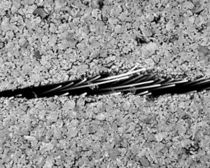 Immagine fotorealistica di un provino di calcestruzzo fibro-rinforzato (PPFRC) di tipo SCB durante una prova di frattura in laboratorio, obiettivo macro 100mm, alta definizione della texture del calcemento e delle fibre esposte lungo la crepa, illuminazione controllata da laboratorio, messa a fuoco precisa sulla propagazione della frattura.