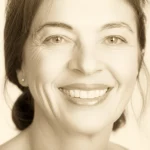 Un ritratto di una donna matura sorridente e in salute, che simboleggia il benessere in postmenopausa grazie alla comprensione del ruolo degli estrogeni. Obiettivo prime da 35mm, con una leggera profondità di campo per mettere a fuoco il suo viso espressivo, utilizzando una palette di colori duotone caldo (es. seppia e crema) per un'atmosfera positiva e rassicurante.