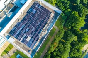Fotografia aerea con drone di un moderno edificio universitario con un esteso impianto fotovoltaico sul tetto che combina pannelli monocristallini (neri), policristallini (bluastri) e a film sottile (neri uniformi), luce solare diretta del primo pomeriggio, alta risoluzione, dettagli nitidi dell'installazione e dell'ambiente circostante verdeggiante tipico della Malesia.