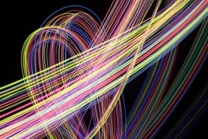 Visualizzazione macro fotorealistica di catene polimeriche colorate e luminose che si intrecciano dinamicamente, a simboleggiare i multinetwork polimerici entangled, con un fascio di luce che ne illumina una sezione, suggerendo l'attivazione tramite luce. Obiettivo macro 90mm, illuminazione controllata ad alto dettaglio, sfondo scuro per enfatizzare la luminescenza.