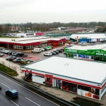 A wide-angle shot of a busy Dutch motorway service area, showing various food outlets and parked cars, capturing the overall environment. Landscape wide angle 10mm, sharp focus.
