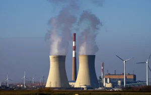 Immagine fotorealistica di ciminiere di una centrale elettrica cinese da cui esce vapore pulito invece di fumo scuro, con sullo sfondo un cielo sereno e turbine eoliche in lontananza, a simboleggiare la transizione energetica. Scatto con teleobiettivo zoom 100mm, luce del tardo pomeriggio, alta definizione, fast shutter speed.
