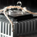 Un primo piano di un MOSFET SiC montato su un dissipatore di calore in alluminio, con corde di cotone umide che lo avvolgono e gocce d'acqua che evaporano. L'immagine è scattata con un obiettivo macro da 90mm per evidenziare i dettagli del processo di evaporazione, con illuminazione controllata e un leggero effetto di vapore. High detail, precise focusing.