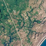 Veduta aerea satellitare di un paesaggio diversificato che mostra aree verdi lussureggianti e zone aride colpite dalla siccità, con fiumi e laghi visibili. Obiettivo grandangolare 14mm, alta risoluzione, luce naturale del giorno, per illustrare il concetto di valutazione della siccità basata su satellite e l'integrazione di AHP e logica fuzzy.