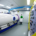 Interno di una camera iperbarica clinica moderna, vista grandangolare 18mm, illuminazione controllata, con dettagli visibili dei sistemi di monitoraggio e erogazione ossigeno, atmosfera serena e tecnologica, un tecnico osserva un pannello di controllo.