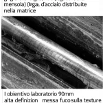 Primo piano di una sezione trasversale di una trave a mensola in calcestruzzo UHPFRC grigio chiaro, mostrando le barre di armatura interne (legacci della mensola) e le fibre d'acciaio distribuite nella matrice. Illuminazione da laboratorio controllata, obiettivo macro 90mm, alta definizione, messa a fuoco precisa sulla texture del calcestruzzo e sull'acciaio.