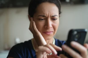 35mm portrait, depth of field, showing a young or middle-aged person looking at a smartphone with a pained expression, background slightly blurred.