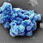Macro fotografia, 60mm lens, di brillanti nanoaggregati cristallini blu e verdi che rappresentano le particelle del catalizzatore di molibdato di zirconio su una superficie scura e texturizzata, messa a fuoco precisa, illuminazione drammatica controllata, alto dettaglio.