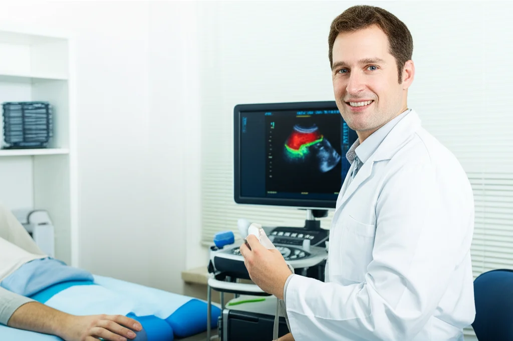 Ritratto ambientato di un fisioterapista sorridente che utilizza un'ecografo portatile per misurare la rigidità muscolare sulla schiena bassa di un paziente sdraiato prono su un lettino in uno studio moderno e luminoso. Messa a fuoco sul volto del fisioterapista e sullo schermo dell'ecografo che mostra un'immagine colorata di elastografia. Obiettivo prime 35mm, profondità di campo media, luce naturale laterale.