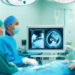 Immagine fotorealistica di un'équipe medica in sala operatoria che discute davanti a uno schermo che mostra una TC-angiografia dell'aorta e delle arterie iliache di un paziente candidato al trapianto di rene. L'immagine sullo schermo evidenzia le calcificazioni. Obiettivo prime 24mm, profondità di campo per includere l'équipe e lo schermo a fuoco, illuminazione da sala operatoria.