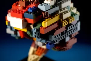Una composizione artistica di mattoncini LEGO di varie forme e colori disposti a formare un cervello stilizzato, simboleggiando la creatività e l'applicazione scientifica. Illuminazione da studio drammatica, obiettivo macro 100mm, alta definizione, focus selettivo sulla texture dei mattoncini.