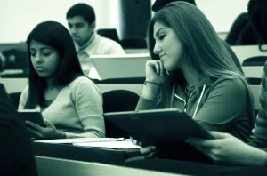 Studenti universitari in un'aula pakistana, intenti a utilizzare laptop e tablet, simboleggiando l'integrazione di ChatGPT nell'istruzione superiore. L'immagine dovrebbe trasmettere un senso di modernità e concentrazione. Prime lens, 35mm, depth of field, luce naturale, duotone verde acqua e grigio scuro.