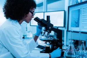 Un ricercatore in un laboratorio moderno osserva campioni di siero attraverso un microscopio avanzato, con schermi che mostrano dati metabolomici sullo sfondo. Illuminazione da laboratorio, obiettivo prime 35mm, duotone blu e grigio per un'atmosfera scientifica e high-tech.