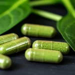 Primo piano macro con lente da 90mm di capsule di integratori di acido folico sparse accanto a verdure a foglia verde scuro come spinaci, illuminazione controllata per evidenziare i dettagli.