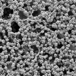 Immagine fotorealistica di un campione di materiale granulare umido analizzato con microtomografia a raggi X, evidenziando la complessa interazione tra particelle solide e fase liquida, con ponti liquidi visibili, illuminazione da studio, obiettivo macro 100mm, alta definizione e focus preciso sulla microstruttura.