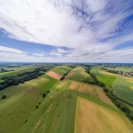 Paesaggio grandangolare, obiettivo 10mm, vista aerea di un terreno variegato che mostra diverse tipologie di suolo (da arido a umido) e vegetazione sotto un cielo con nuvole morbide da lunga esposizione, messa a fuoco nitida su tutto il panorama, colori naturali.