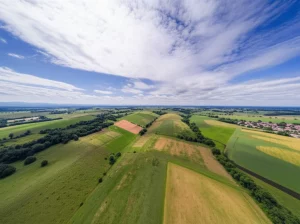 Paesaggio grandangolare, obiettivo 10mm, vista aerea di un terreno variegato che mostra diverse tipologie di suolo (da arido a umido) e vegetazione sotto un cielo con nuvole morbide da lunga esposizione, messa a fuoco nitida su tutto il panorama, colori naturali.