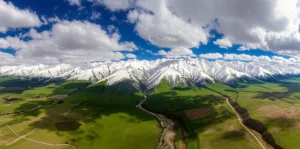 Fotografia aerea grandangolare 10mm dell'altopiano del Qinghai, che mostra montagne innevate e valli verdi sotto un cielo parzialmente nuvoloso, lunga esposizione per nuvole soffici, alta definizione, illuminazione naturale vivida, stile fotorealistico.