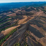landscape wide angle 10mm, sharp focus, aerial view of a forest fire scar in Oregon, patches of green fire refugia visible amongst brown burned areas, clear sky