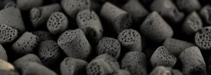 Fotografia macro con lente da 100mm di pellet di biochar nero derivato da letame di pollo. Illuminazione laterale controllata per esaltare la texture porosa e irregolare della superficie. Alta definizione, messa a fuoco selettiva sulla parte anteriore dei pellet, sfondo leggermente sfocato.