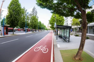 Photorealistic image using a wide-angle lens, 24mm, showing a modern, well-designed urban street with dedicated bike lanes, sidewalks, trees, and public transport stops, illustrating sustainable urban design impacting commuting.