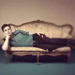A thoughtful individual lying on a classic psychoanalyst's couch in a softly lit room, with a dream-like, slightly blurred background suggesting the realm of the unconscious. The focus is on the person's contemplative expression. Prime lens, 35mm, depth of field, duotone in sepia and muted teal.