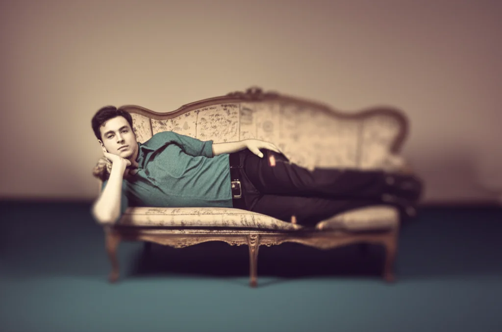 A thoughtful individual lying on a classic psychoanalyst's couch in a softly lit room, with a dream-like, slightly blurred background suggesting the realm of the unconscious. The focus is on the person's contemplative expression. Prime lens, 35mm, depth of field, duotone in sepia and muted teal.