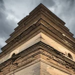 Immagine fotorealistica di un'antica pagoda cinese in mattoni, parzialmente diroccata, che si erge contro un cielo suggestivo. Obiettivo grandangolare 20mm, luce naturale diffusa, alta definizione dei dettagli della muratura e delle crepe.