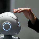 A photorealistic image showing a human hand gently touching a friendly-looking robot's head, illustrating the emotional connection shaped by design, 35mm portrait, depth of field.