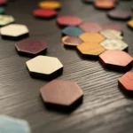 Una composizione artistica di tessere esagonali colorate sparse su un tavolo di legno scuro, con alcune disposte a formare l'inizio di un puzzle scorrevole. Prime lens, 35mm, depth of field, illuminazione calda e invitante che crea ombre morbide, texture delle tessere ben visibile.