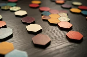Una composizione artistica di tessere esagonali colorate sparse su un tavolo di legno scuro, con alcune disposte a formare l'inizio di un puzzle scorrevole. Prime lens, 35mm, depth of field, illuminazione calda e invitante che crea ombre morbide, texture delle tessere ben visibile.