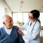 Un medico geriatra sorridente mentre esegue un test di valutazione della mobilità (come l'SPPB) su un residente anziano in una luminosa sala comune di una casa di riposo, obiettivo 50mm, luce naturale, profondità di campo, atmosfera positiva e rassicurante.