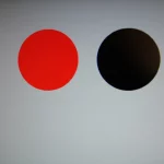 A still life image of a computer monitor displaying two simple circles, one red and one black, on a grey background, macro lens, 100mm, precise focusing, controlled lighting.