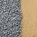 Close-up macro lens 60mm shot of fine recycled concrete aggregate particles next to natural sand, illustrating the difference in texture and color, with precise focusing.