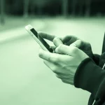 Immagine concettuale di un adolescente che spegne le notifiche del cellulare per andare a correre in un parco. Prime lens, 35mm, duotone verde e grigio, profondità di campo che mette a fuoco l'azione di spegnere il telefono e lo sfondo naturale.