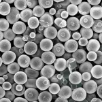 Immagine macro fotorealistica di un aggregato di microsfere polimeriche di due tipi diversi, alcune emettono una debole fosforescenza bluastra mentre altre sono opache. Le sfere sono in stretto contatto, suggerendo attrazione elettrostatica. Illuminazione da studio controllata per evidenziare texture e luminescenza, obiettivo macro 90mm, alta definizione, sfondo scuro e pulito.