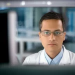 A thoughtful veterinary researcher examining data on a computer screen in a lab, 35mm portrait, depth of field, controlled lighting.