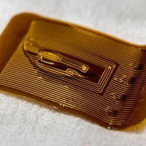 Photorealistic image, macro lens, 100mm, high detail, controlled lighting: Un cerotto biosensore organico Bio-FET potenziato con MXene, realizzato su carta, per il rilevamento del glucosio nel sudore. L'immagine mostra gli strati intricati di PEDOT:PSS, il composito di MXene e il substrato di carta. Il cerotto è flessibile e leggermente piegato, con minuscoli elettrodi visibili. Una singola gocciolina di sudore si trova sull'area del sensore.