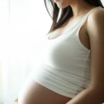 A woman looking thoughtfully at her pregnant belly, 35mm portrait, soft natural light, depth of field, symbolizing the start of a health journey.