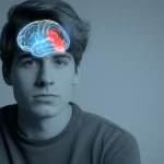 Immagine concettuale del cervello umano con l'amigdala illuminata, sovrapposta a un ritratto stilizzato di un giovane con espressione neutra. Utilizzo di un obiettivo da 35mm per un effetto ritratto, con duotone blu e grigio per un'atmosfera introspettiva e scientifica, profondità di campo.