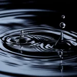 Fotografia macro di gocce d'acqua che cadono sulla superficie increspata di un pozzo sotterraneo scuro, illuminazione controllata per enfatizzare la texture dell'acqua e la profondità, obiettivo macro 90mm, alta definizione.