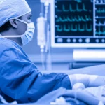 Primo piano, obiettivo prime 35mm, di un cardiochirurgo pediatrico che esamina attentamente i dati di un monitor in sala operatoria durante un intervento al cuore su un neonato (modello o contesto simulato), luce controllata, profondità di campo che sfoca lo sfondo, toni duotone blu e grigio per un'atmosfera clinica ma concentrata.